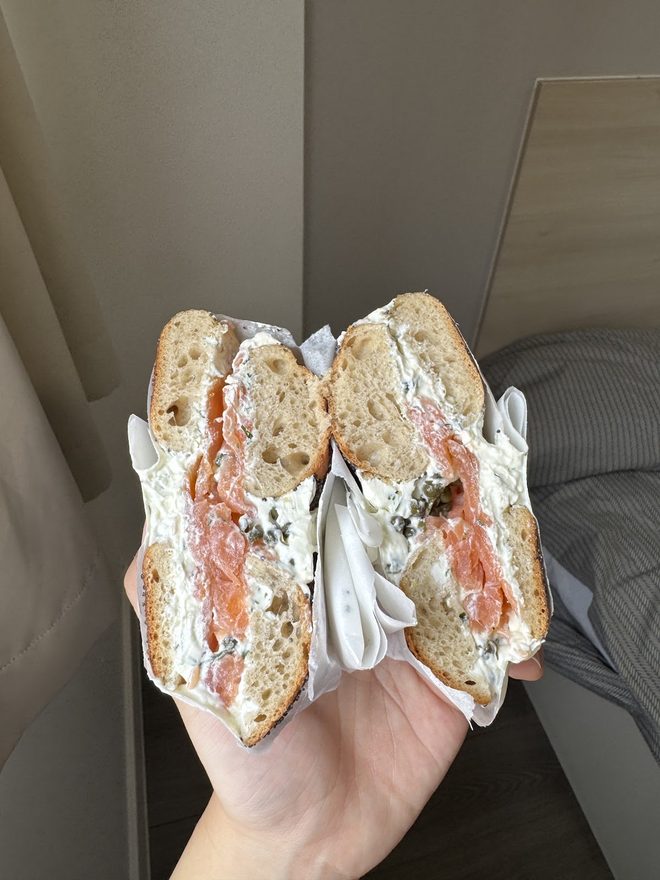 A hand holding a salmon and cream cheese bagel