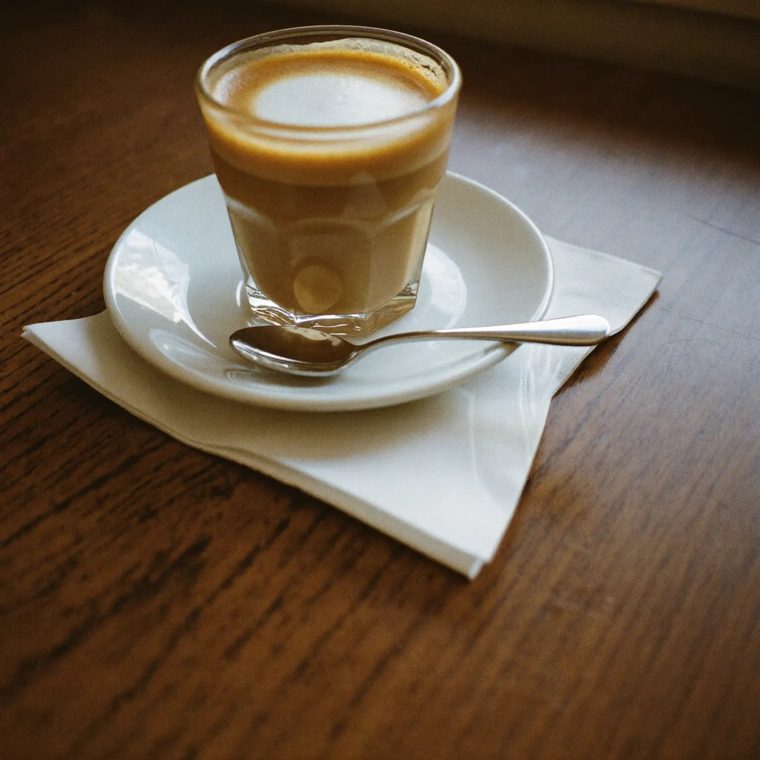 A cortado in a small glass on a wooden table